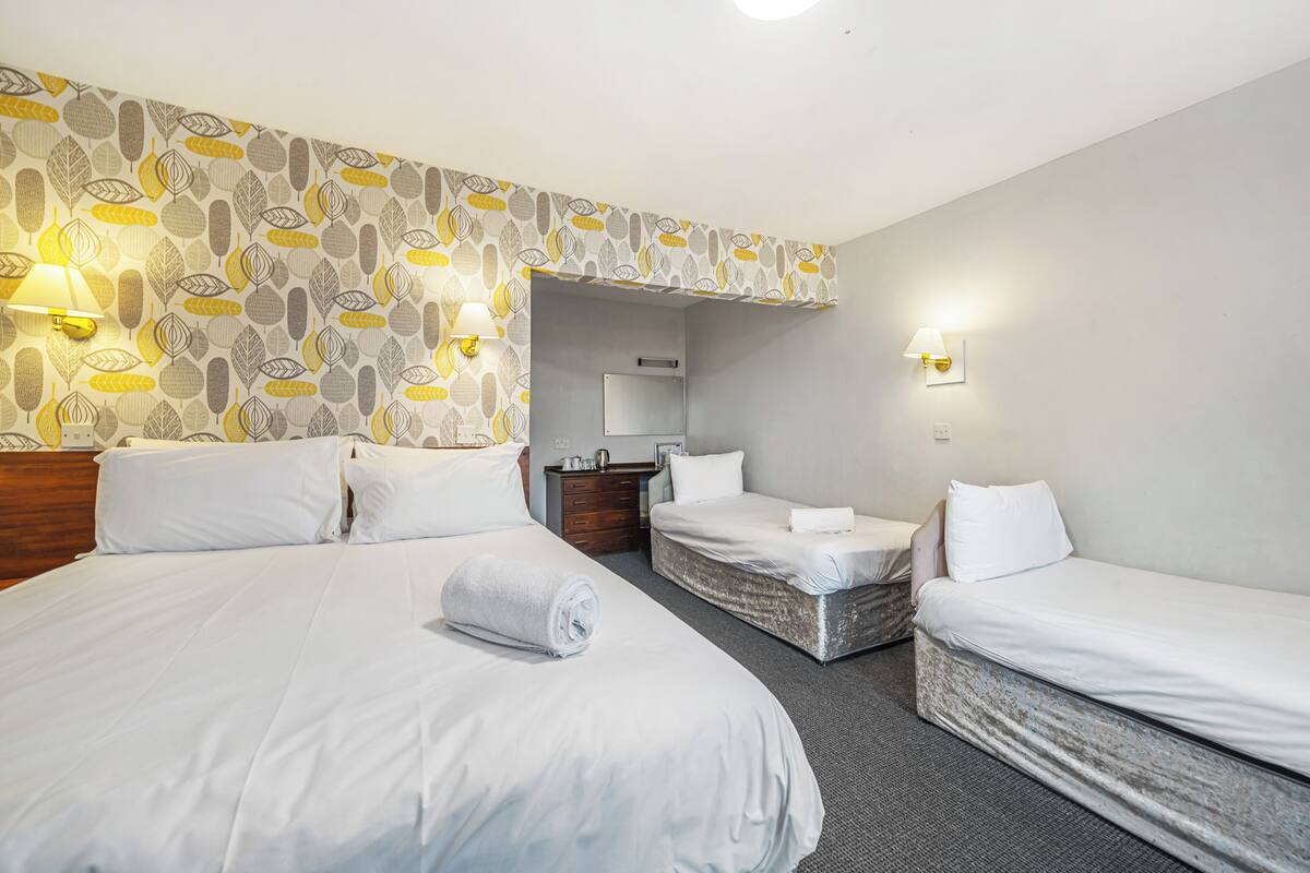A hotel room with three beds, a wooden dresser, and a mirror.