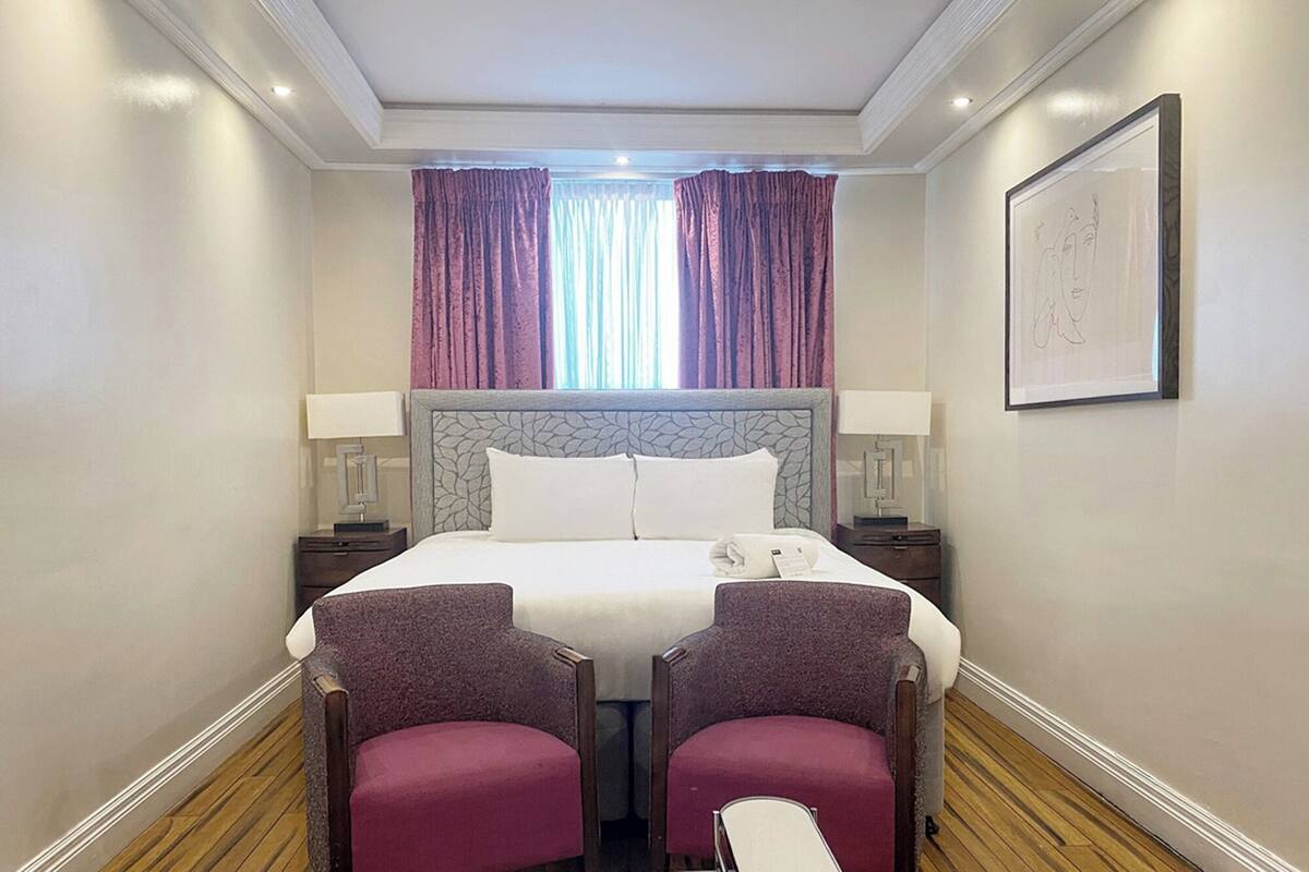 A hotel room with a large bed, two armchairs, a nightstand, and a framed artwork on the wall.