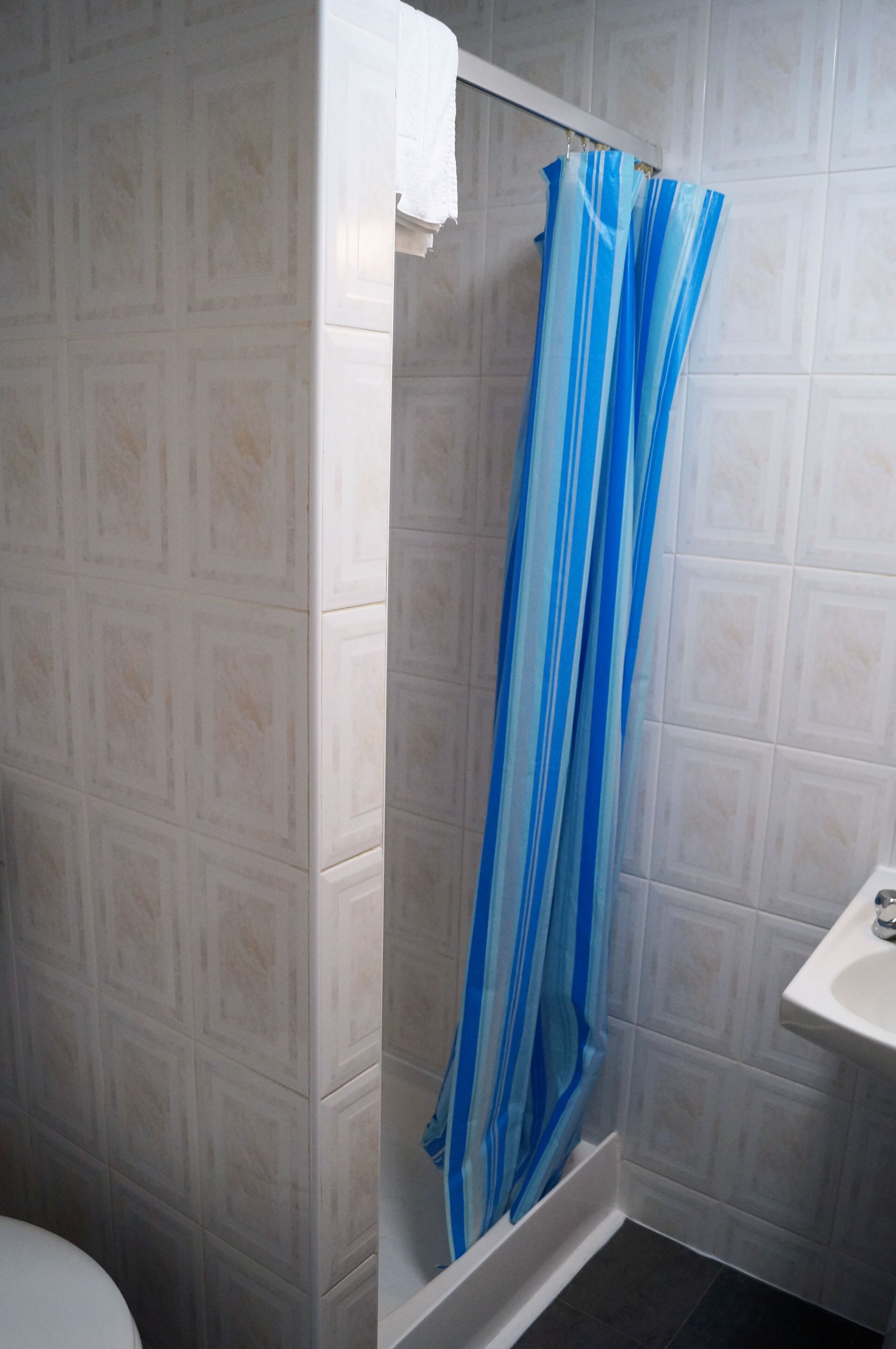 A bathroom with a shower curtain, tiled walls, and a sink.
