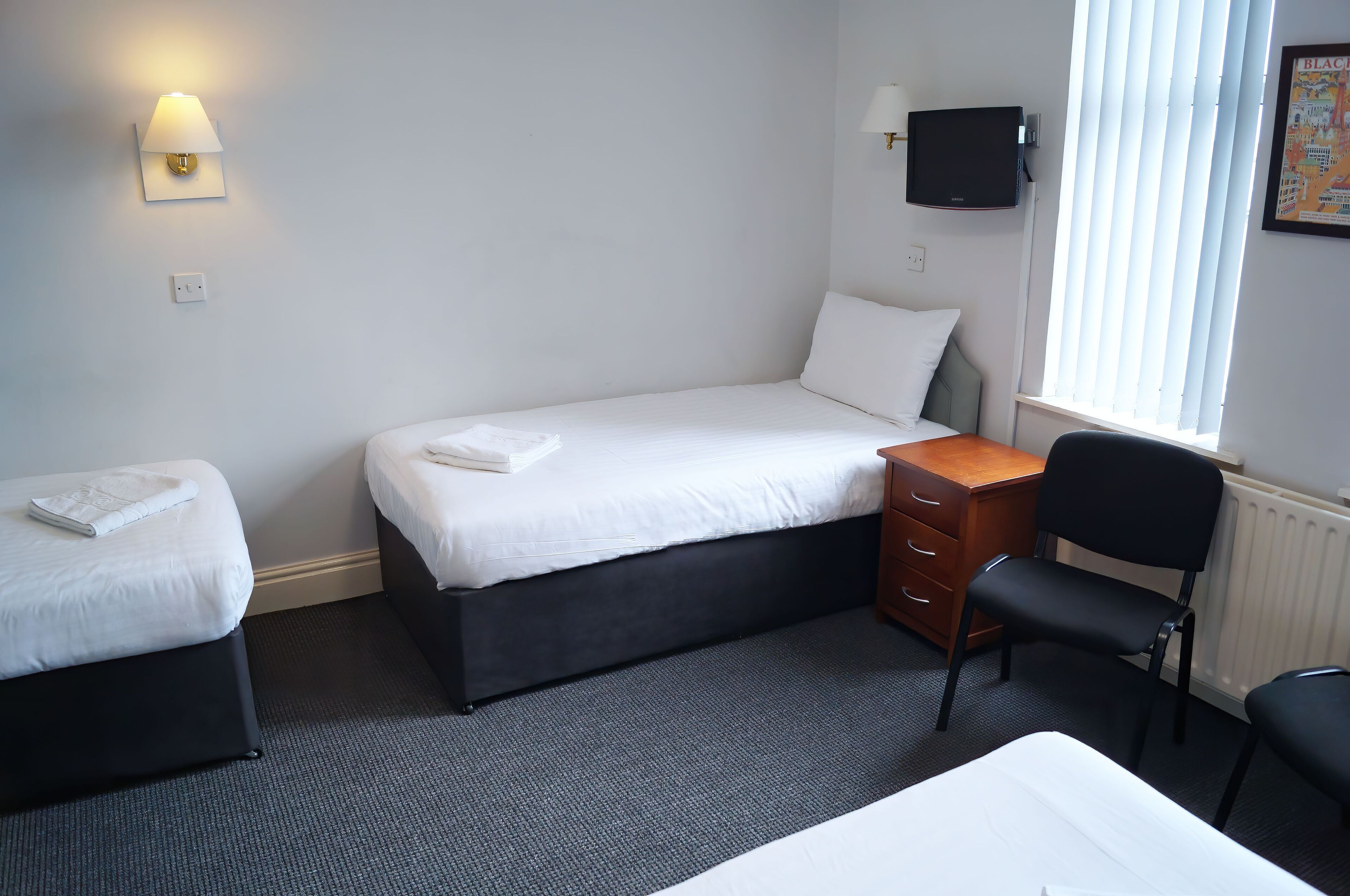 A hotel room with two beds, a desk, a chair, a TV, and a window with blinds.