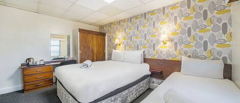 A hotel room with two beds, a wooden dresser, a desk, a mirror, and patterned wallpaper.