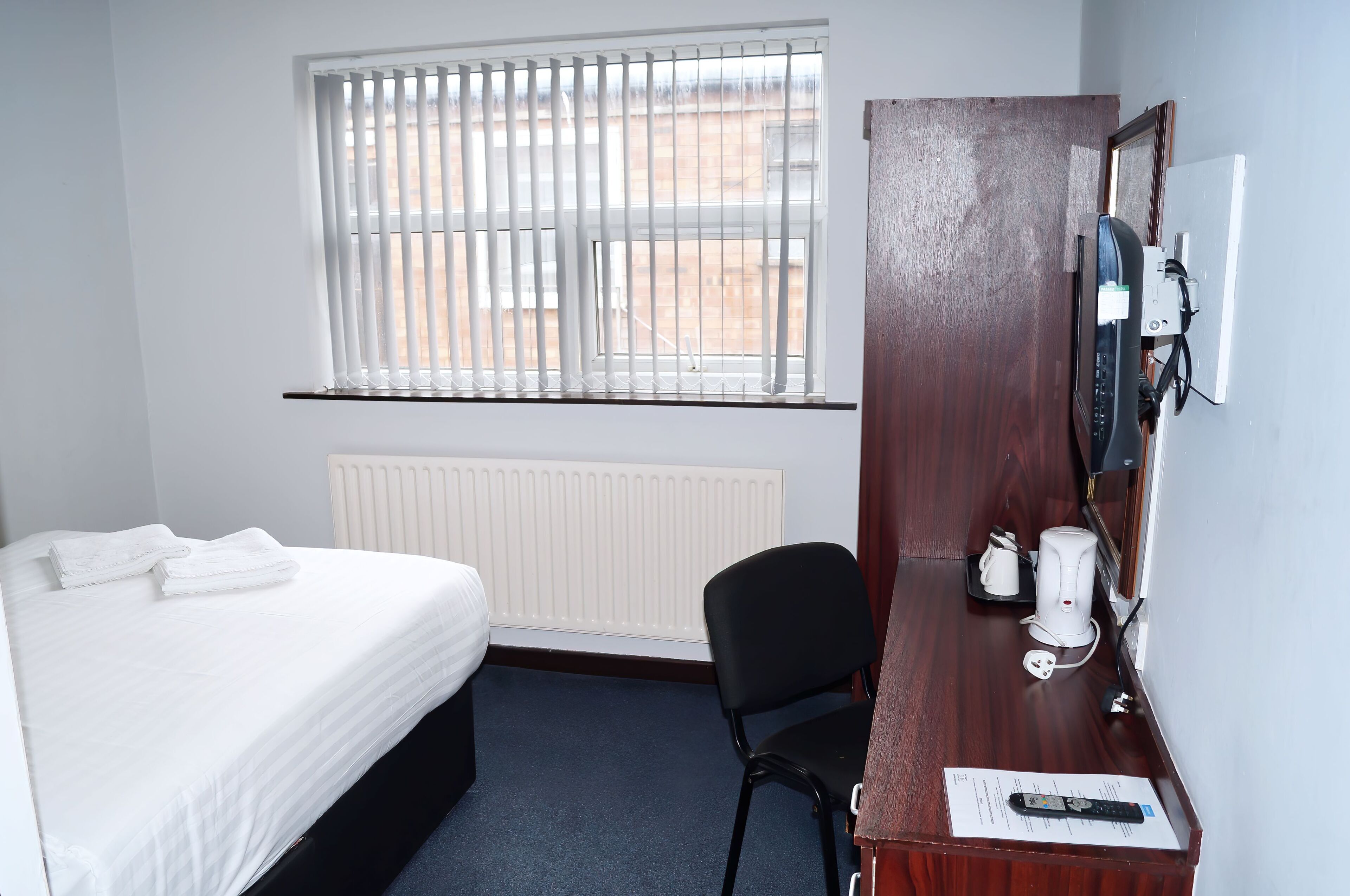 Une chambre d’hôtel comprenant un lit, un bureau avec une chaise, une bouilloire et un radiateur.