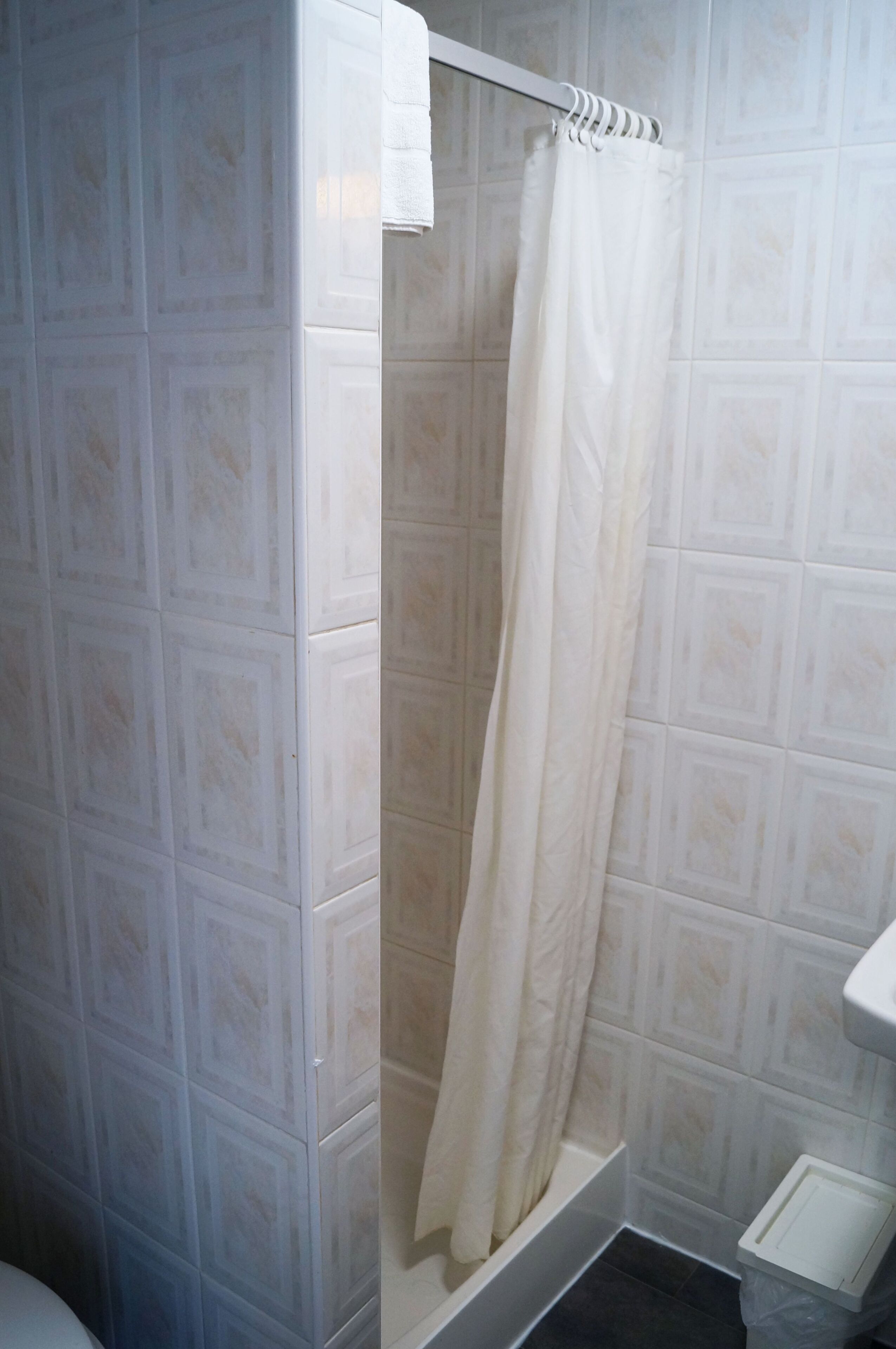 Une salle de bain avec un rideau de douche, des murs carrelés et un lavabo blanc.