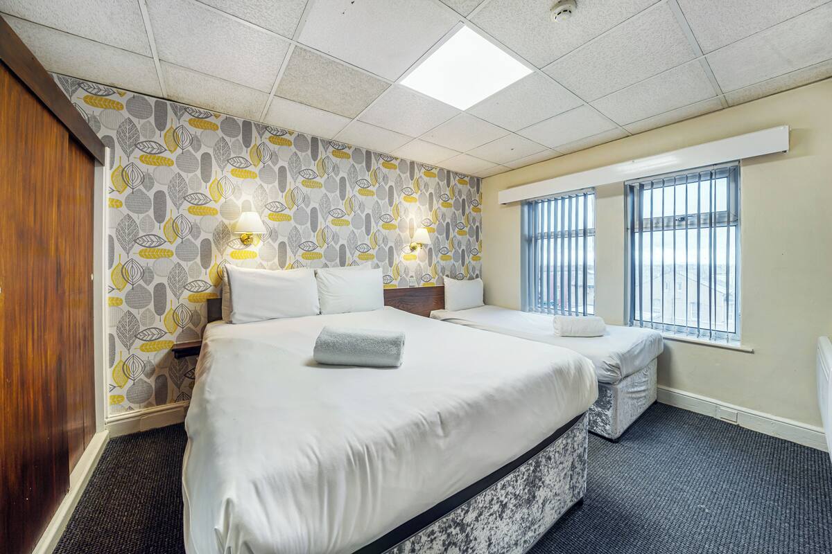A hotel room with a large bed, two bedside tables, a window with bars, and patterned wallpaper.