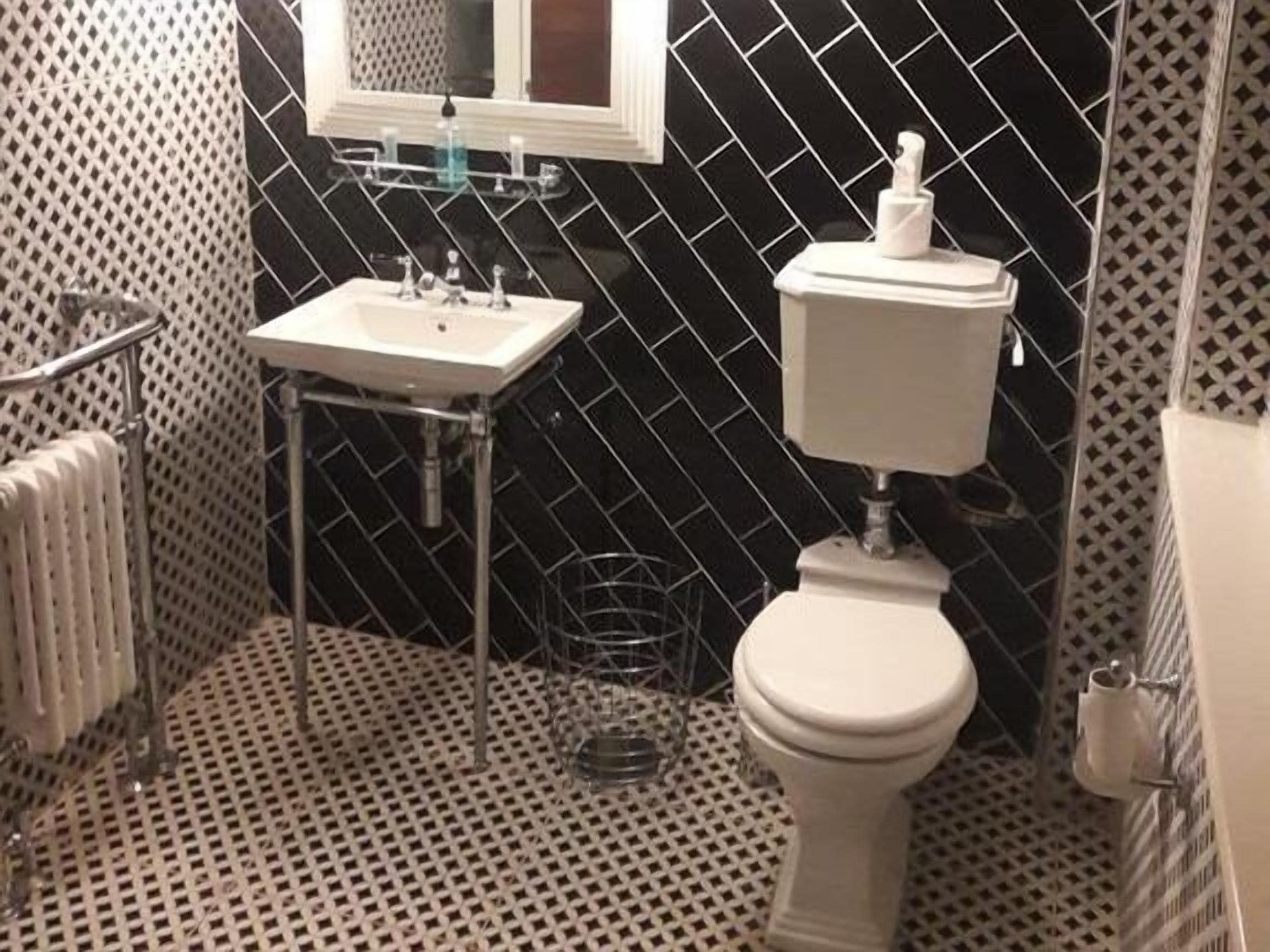 Un baño con piso de baldosas blanco y negro, un lavamanos blanco, un inodoro y un espejo sobre el lavamanos.