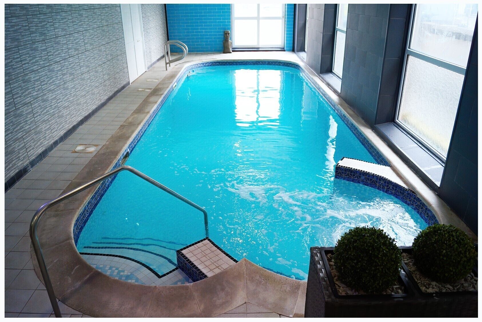 An indoor swimming pool with clear blue water, tiled edges, and a metal ladder.