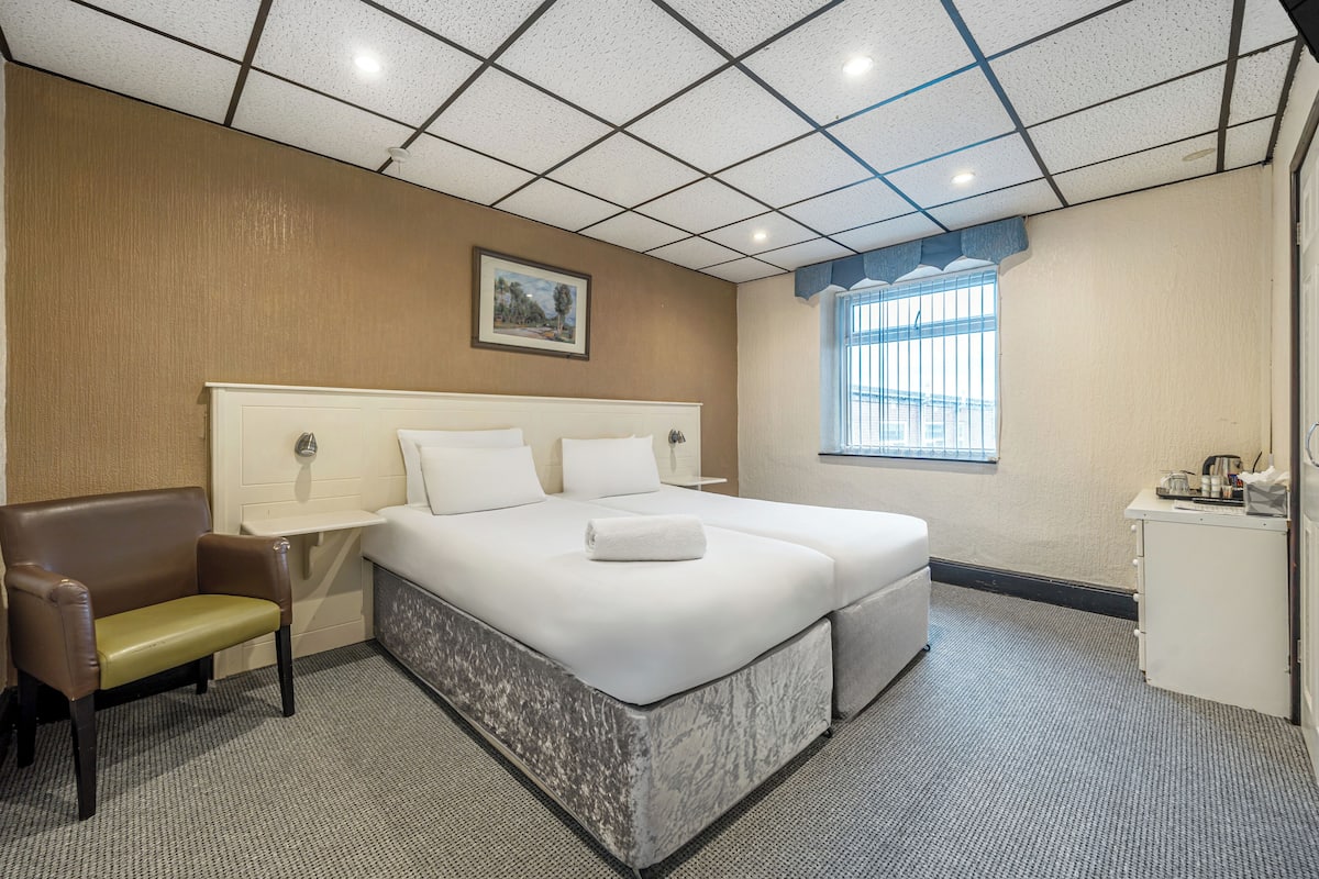 A hotel room with a large bed, a small desk, a chair, and a window.