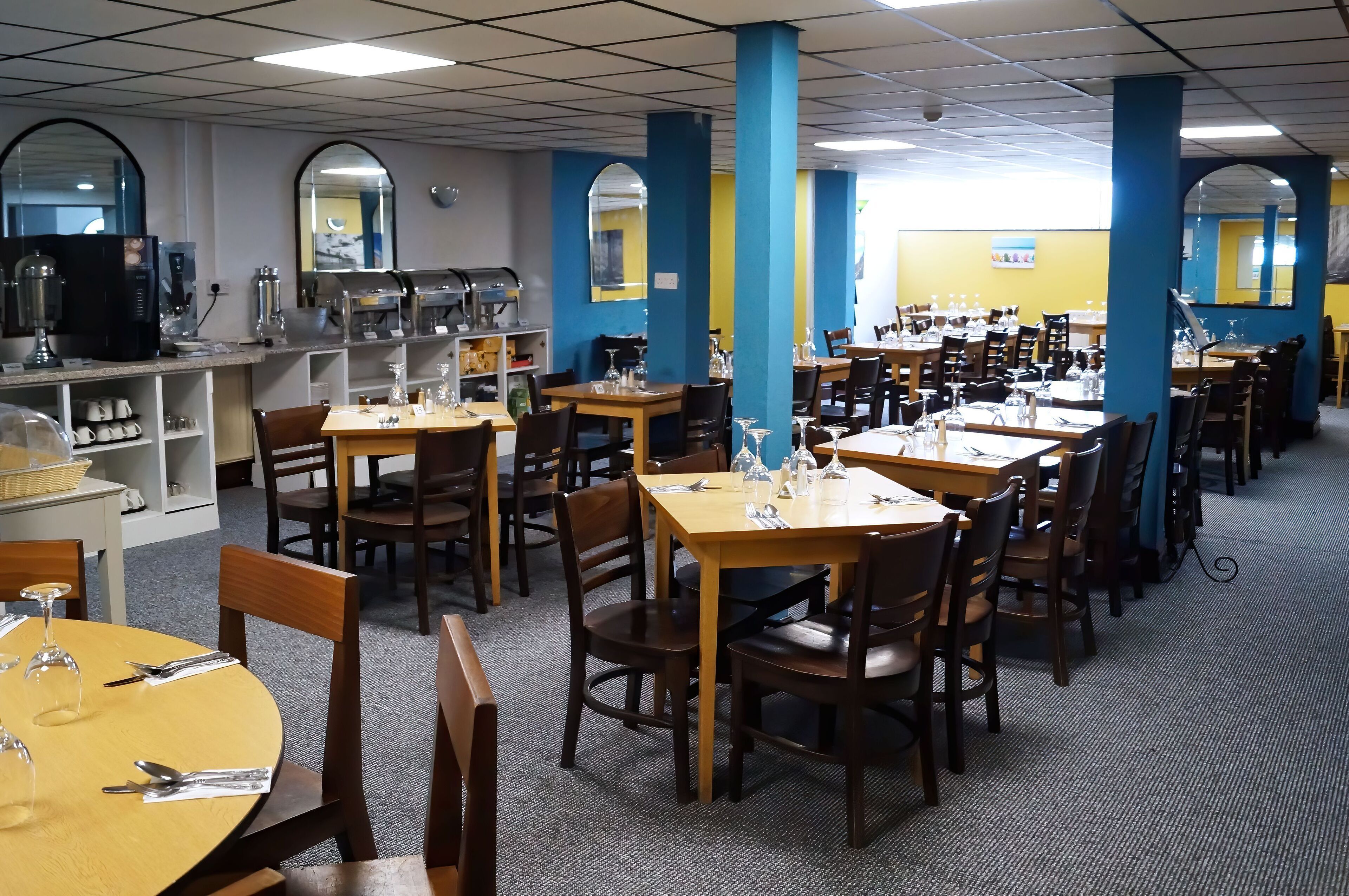 A restaurant with multiple tables and chairs, a coffee machine, and a counter with various items.