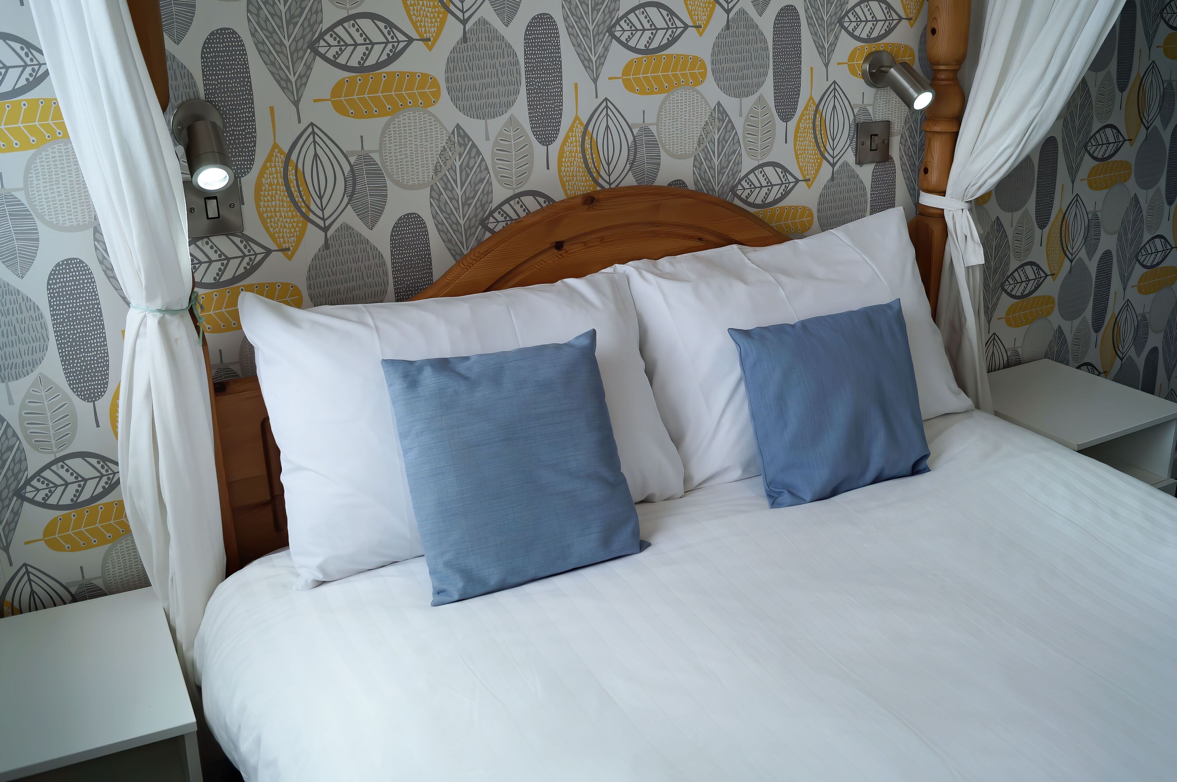 A bed with white and blue pillows, a wooden headboard, and a wall with a leaf pattern.