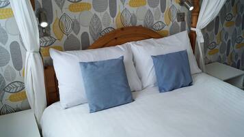 A bed with white and blue pillows, a wooden headboard, and a wall with a leaf pattern.