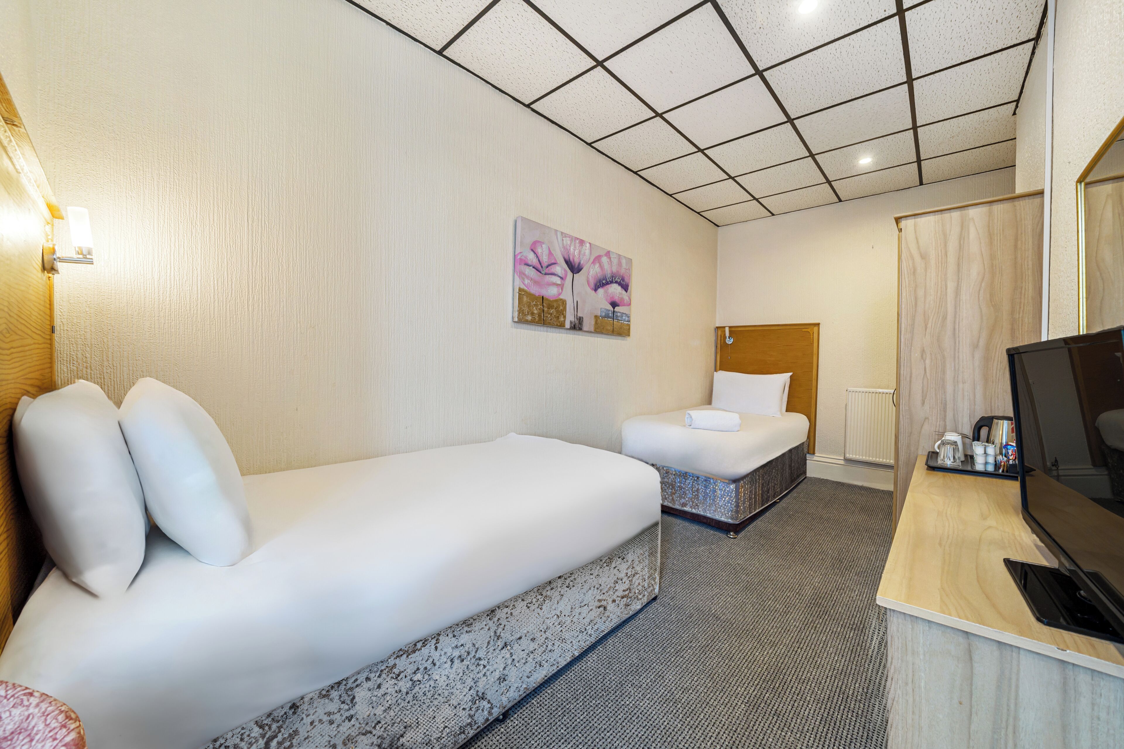 Una habitació d'hotel amb un llit gran, un altre més petit, una taula de treball amb televisió i un quadre a la paret.