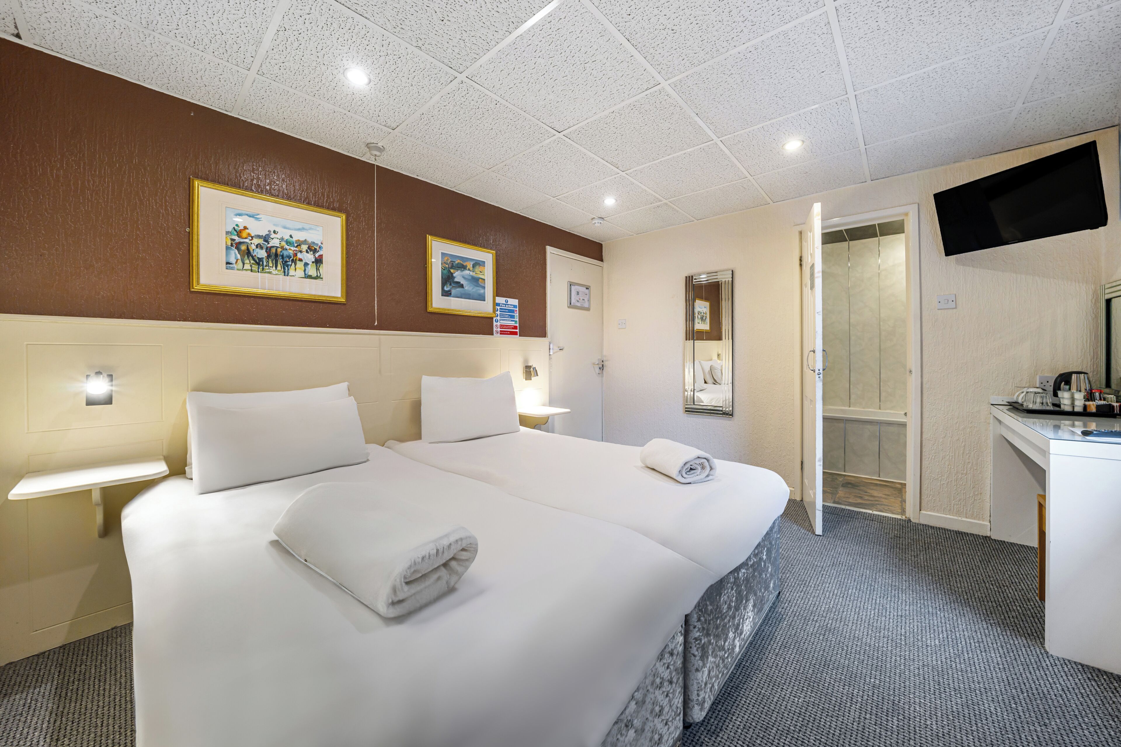 A hotel room with a large bed, bedside tables, a desk, a flat-screen TV, and framed pictures on the wall.
