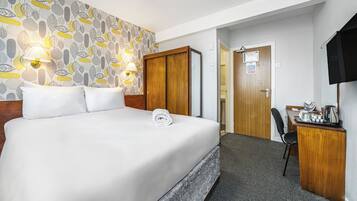 Quarto de hotel com uma cama grande, uma escrivaninha com cadeira, uma televisão e papel de parede estampado.