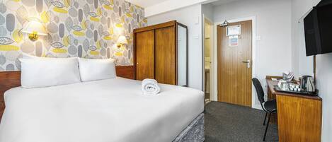 Ein Hotelzimmer mit einem großen Bett, einem Schreibtisch mit Stuhl, einem Fernseher und einer Wand mit Muster.