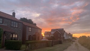 Una calle residencial con casas, un camino de grava y una puesta de sol al fondo.