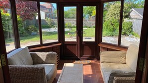 Una sala de estar con mobiliario de mimbre, un ventanal de vidrio que da al exterior y vistas a un jardín trasero.