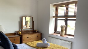 Un dormitorio ordenado con cama, cómoda, espejo y ventana con persianas.