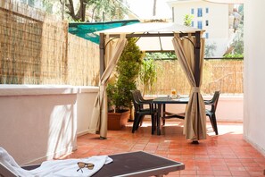 Un patio soleado con mesa y sillas, un espacio de estar techado y una planta en maceta.