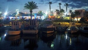 A marina with boats docked, palm trees, and a building with lights in the background. - Andros Apt. 2 Bed, free Wi-Fi, safe, Complex pool (Paralimni)