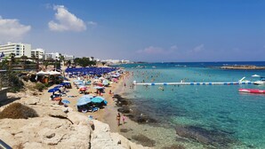 A beach with clear turquoise water, umbrellas, and people. - Andros Apt. 2 Bed, free Wi-Fi, safe, Complex pool (Paralimni)