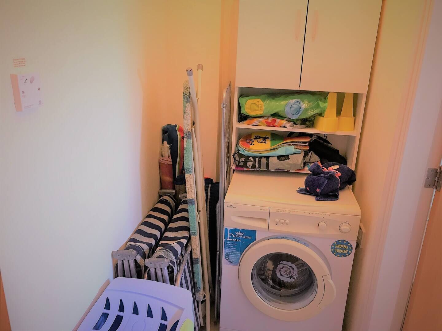 Ein kleiner Hauswirtschaftsraum mit Waschmaschine, Wäscheständer und Regalen mit gefalteter Kleidung.