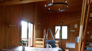 L’intérieur d’un chalet en bois comprend une table à manger, des chaises, un banc, un fauteuil suspendu et un escalier.