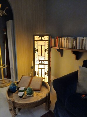 A room with a traditional Chinese paper lantern, a small wooden table with cups and a book, and a bookshelf with books.