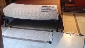 Uma cama com colcha estampada, duas almofadas, uma mesa de cabeceira com abajur e uma parede com padrão geométrico.