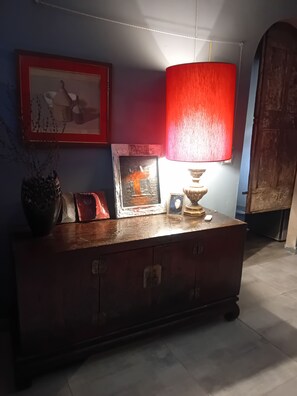 Un aparador de madera con una lámpara roja, un cuadro enmarco y un reloj pequeño.