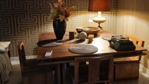 Uma sala de jantar com papel de parede estampado, uma mesa com um vaso de flores, um abajur e uma chaleira.