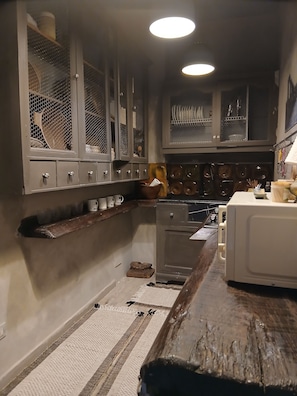 A kitchen with a microwave, stove, and various utensils. There is a wooden shelf and a rug on the floor.