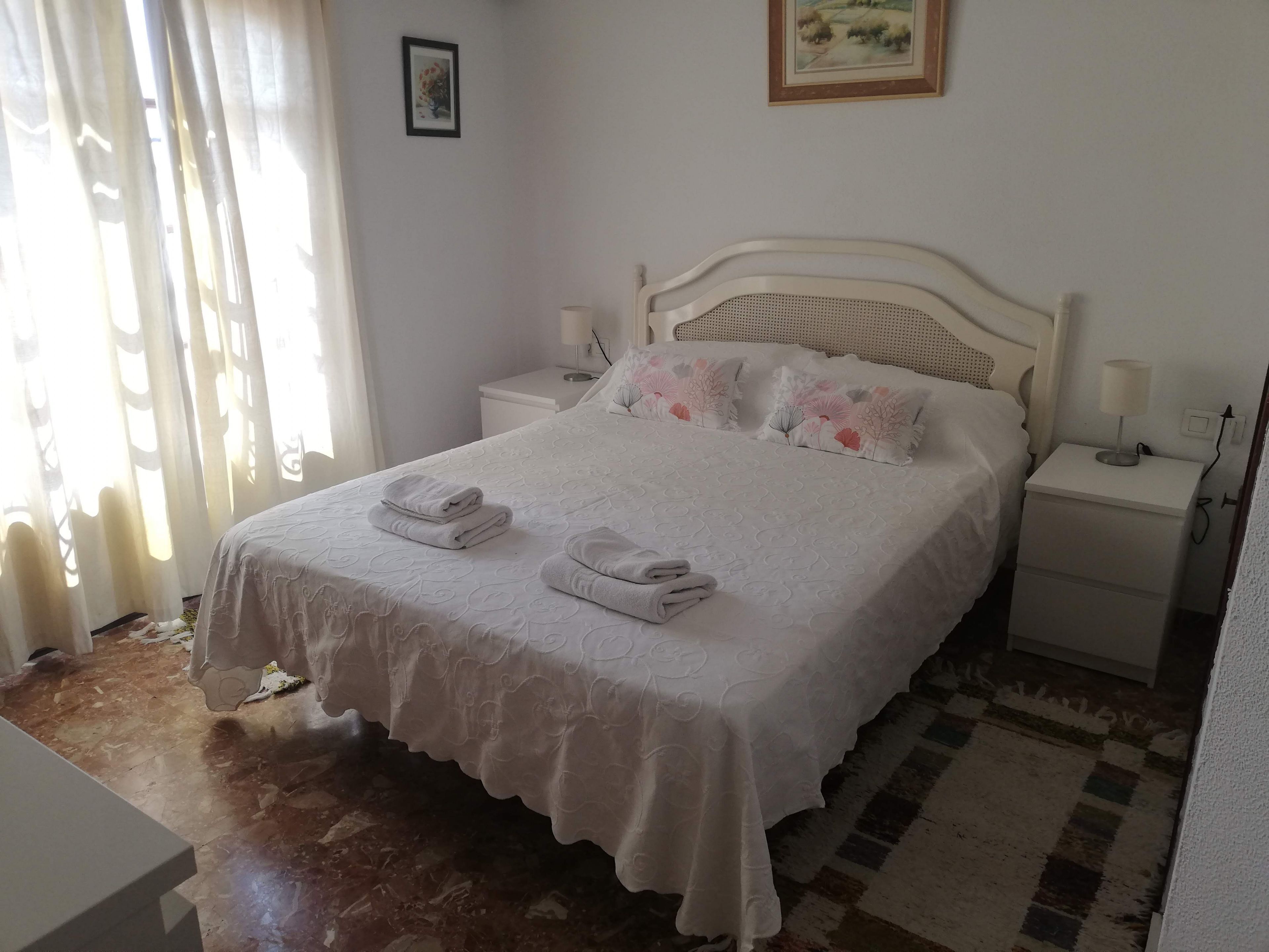 A neatly made bed with folded towels, a bedside table with a lamp, and a patterned rug on the floor.