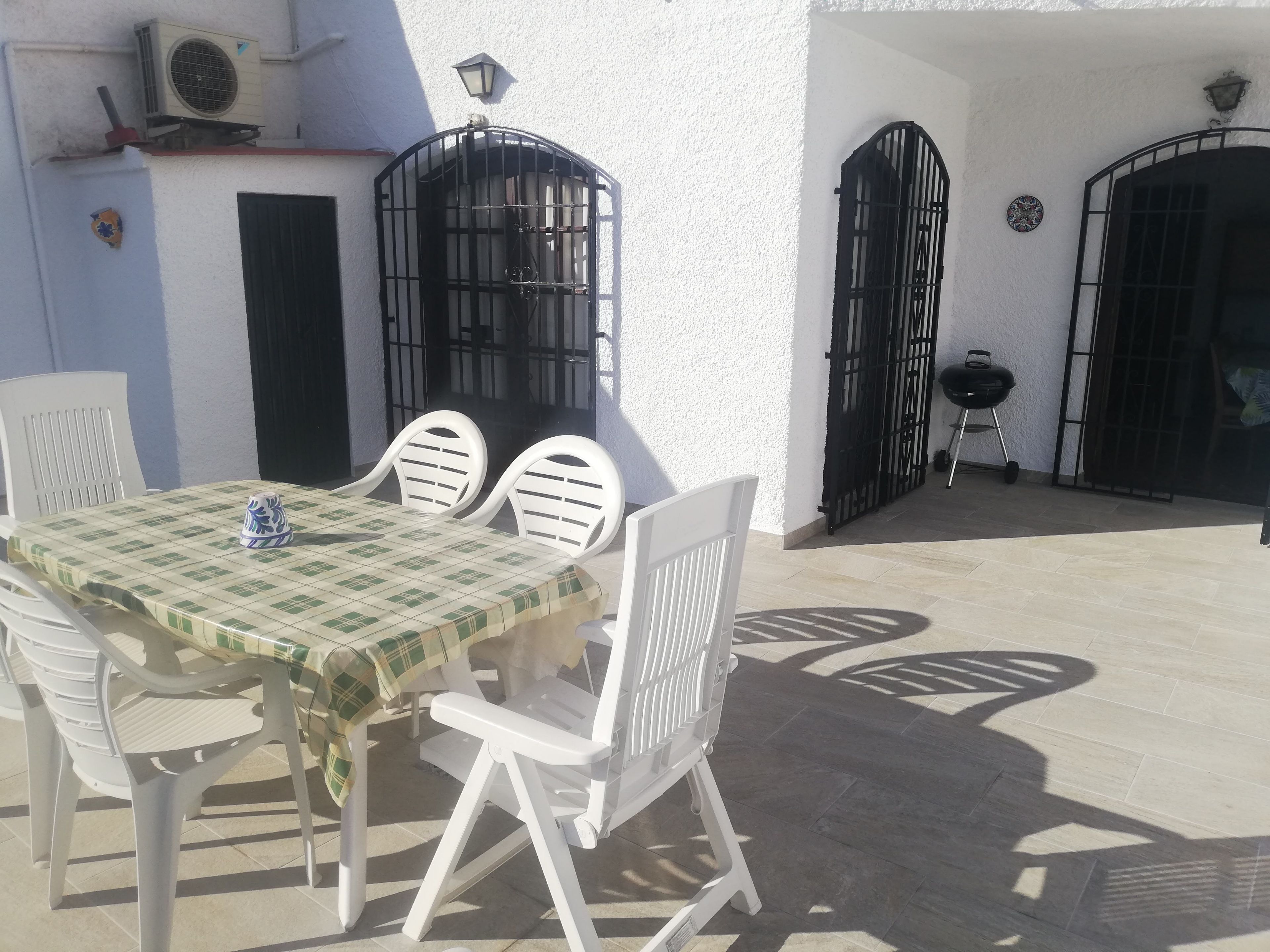 Eine Terrasse im Freien mit Tisch, Stühlen, einem Grill und einer weißen Mauer mit schwarzen Toren.