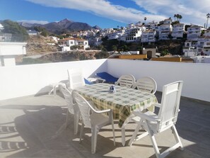 En terrasse med et bord og stole, der giver udsigt over en bakke med hvide bygninger og palmer.