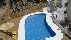 En swimmingpool med en mur av sten och en vitkaklad poolterrass.