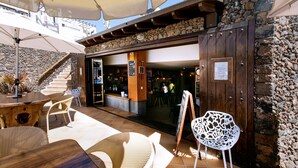 An outdoor seating area with wicker furniture, a stone wall, and a wooden entrance to a restaurant. - Club Oceano 1 bedroom apts. (Puerto del Carmen)