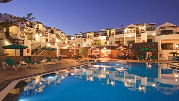 A resort with a swimming pool, outdoor seating, and multiple buildings with balconies. - Club Oceano 1 bedroom apts. (Puerto del Carmen)