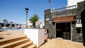 A reception area with a stone facade, a pool in the background, and a clear blue sky. - Club Oceano 1 bedroom apts. (Puerto del Carmen)