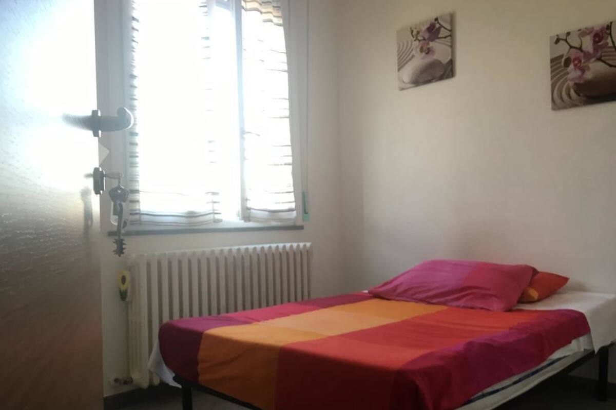 A single bed with a colorful bedspread in a room with a radiator and a window with blinds.