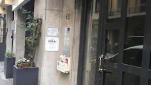 A building entrance with a dark glass door, a concrete wall, and a small mailbox on the right. - B&B Colombo (Pisa)