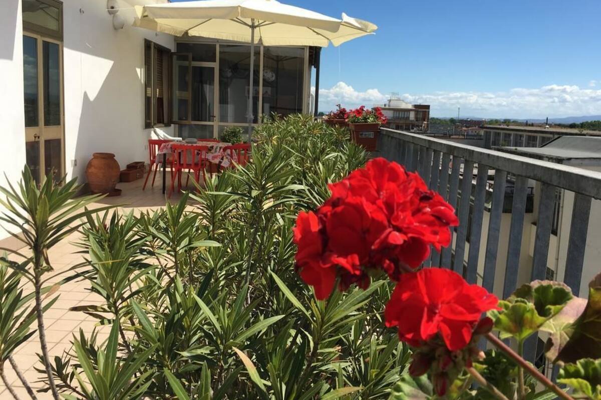 A balcony with red flowers, a table, chairs, and a white umbrella.