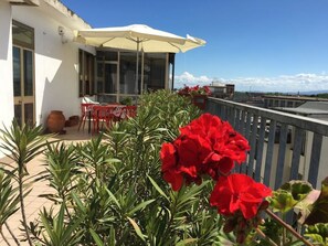 A balcony with red flowers, a table, chairs, and a white umbrella. - B&B Colombo (Pisa)