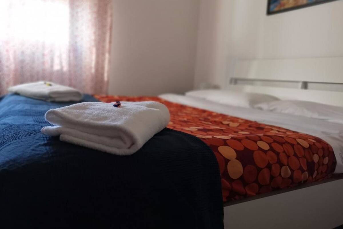 A hotel room with a bed, a blue and red patterned bedspread, and a white towel on the bed.
