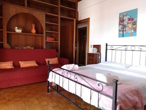 Una habitación con una cama, un sofá rojo, una estantería de madera y un cuadro en la pared.