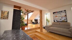 A spacious living area with a high ceiling, a stone accent wall, a wooden staircase, a beige sofa, and a large window.