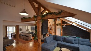 A spacious loft with a large wooden ceiling, a built-in kitchen, a cozy seating area, and a staircase leading to an upper level.