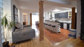A modern kitchen with a central island, bar stools, and a dining area with a sofa and table.