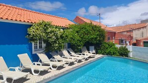 A swimming pool with lounge chairs, a blue building, and a red-tiled roof. - Casa Azul: Tranquility and tranquility in the ocean (Foz do Arelho)