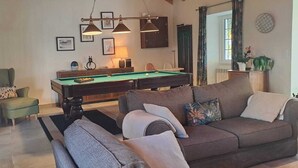 A living room with a pool table, a sofa, and a chair. There are framed pictures on the wall and a lamp on a side table. - Casa Azul: Tranquility and tranquility in the ocean (Foz do Arelho)