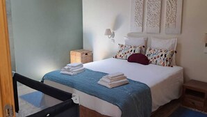 A hotel room with a bed, a nightstand, a small wooden cabinet, and a wicker basket. - Casa Azul: Tranquility and tranquility in the ocean (Foz do Arelho)